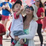 A woman holding a child and waving an american flag.