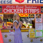 A woman standing in front of a chicken strip stand.