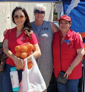 Three women standing next to each other holding a bag of oranges.